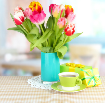 Beautiful tulips in bucket with gifts and cup of tea